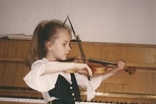 Irena Benak as a young girl playing violin in front of a piano