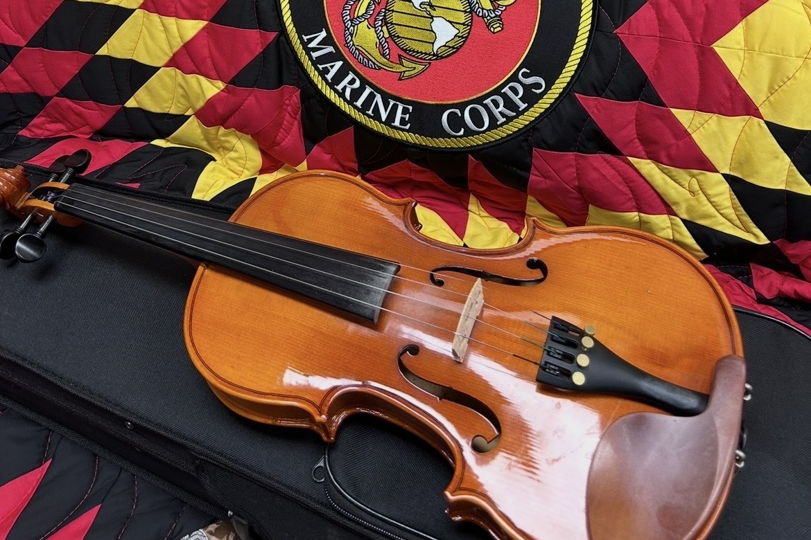 A violin resting on a quilt bearing the U.S. Marine Corps emblem