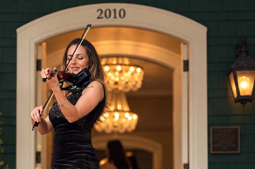 Irena Benak playing violin on the front steps of a venue at a wedding