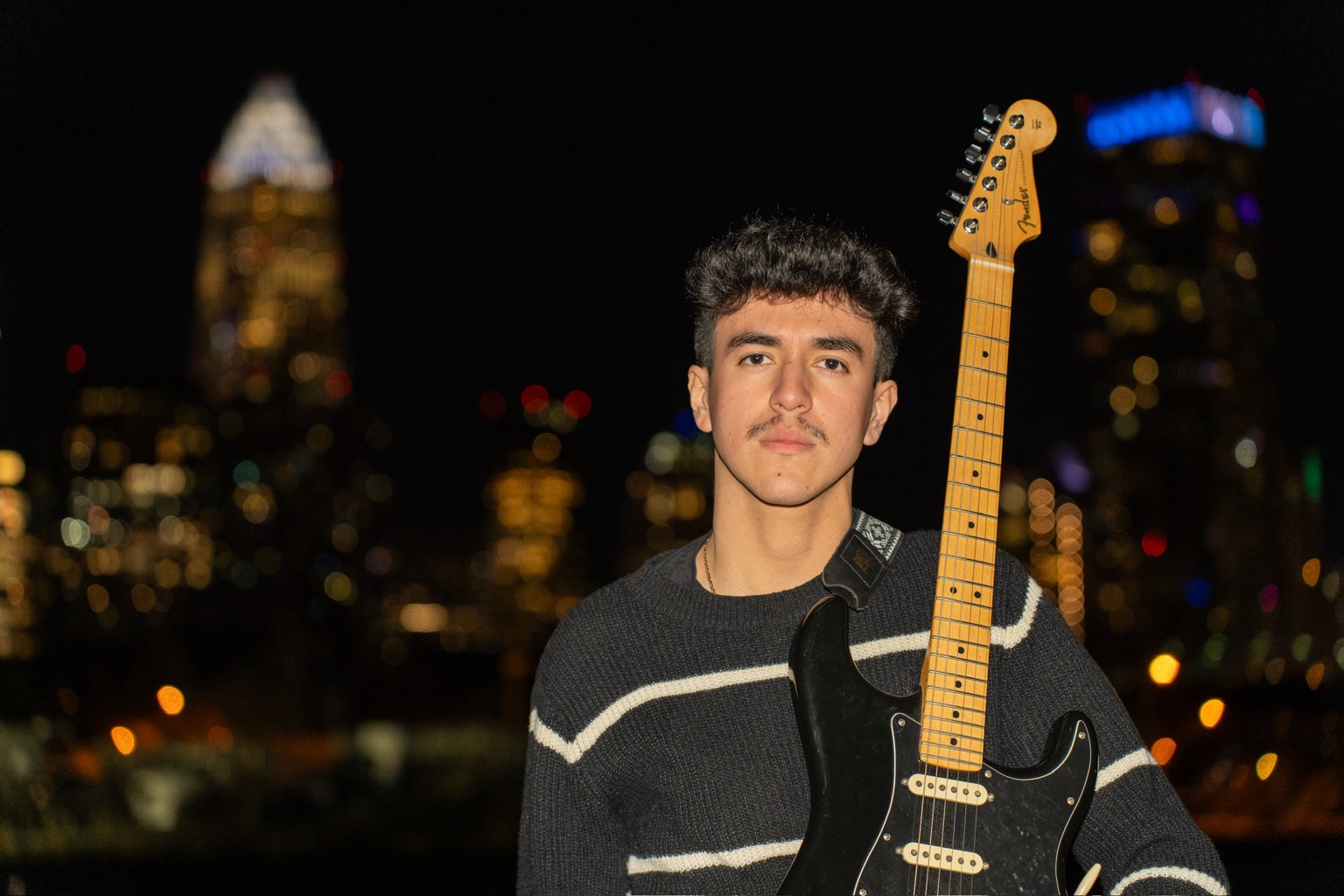 Anthony Vasquez with an electric guitar, Charlotte skyline behind him